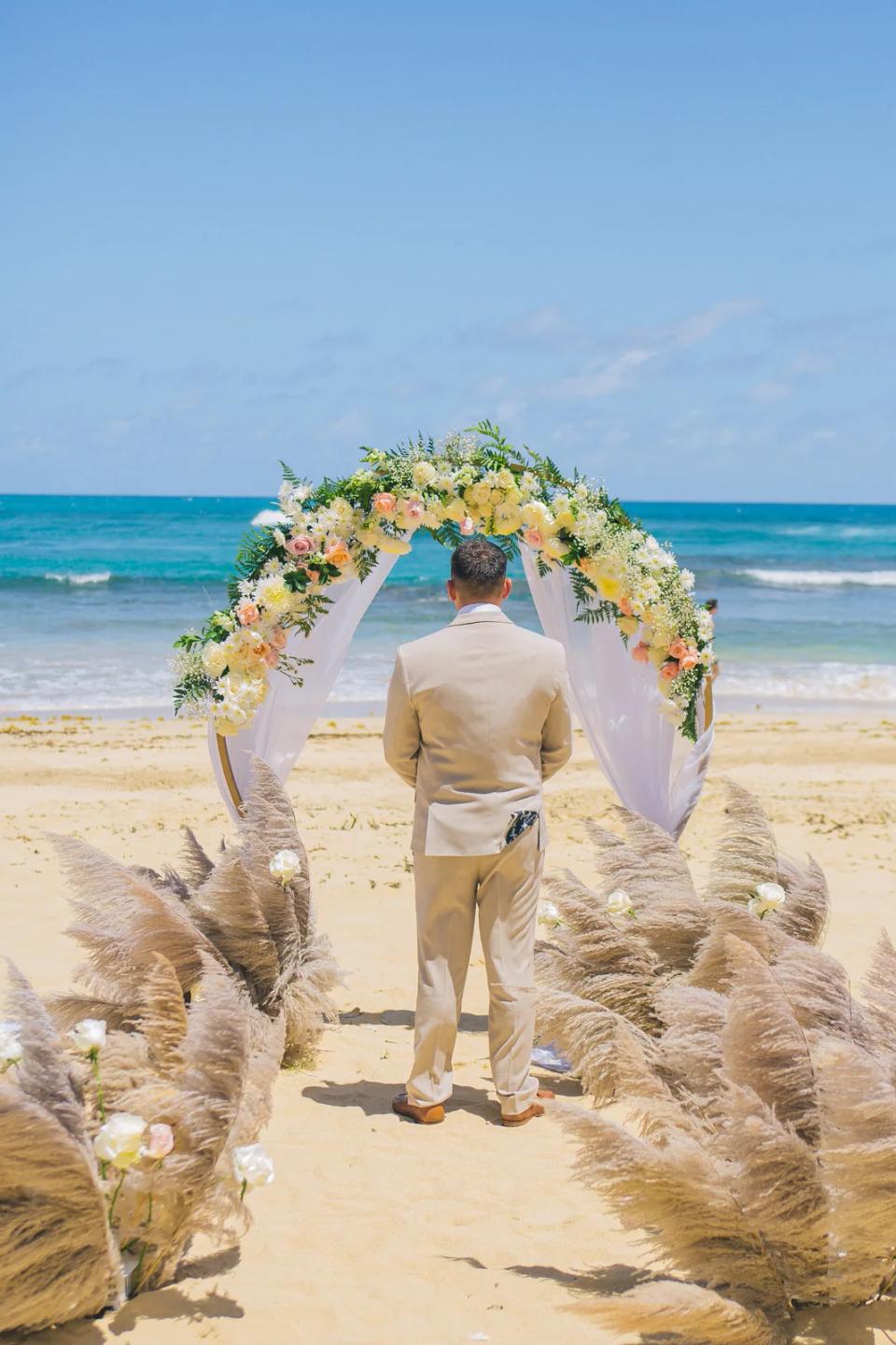 Marié attendant au bout d’une allée de cérémonie bordée de pampas sur une plage de Punta Cana