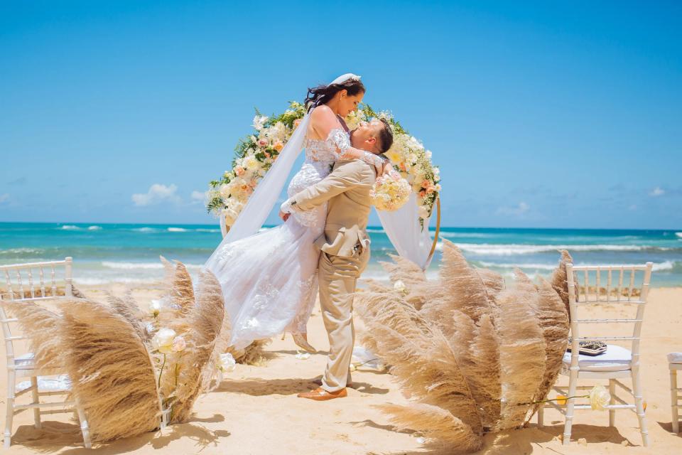 Couple de jeunes mariés sous une arche florale ornée de pampas sur une plage de Punta Cana
