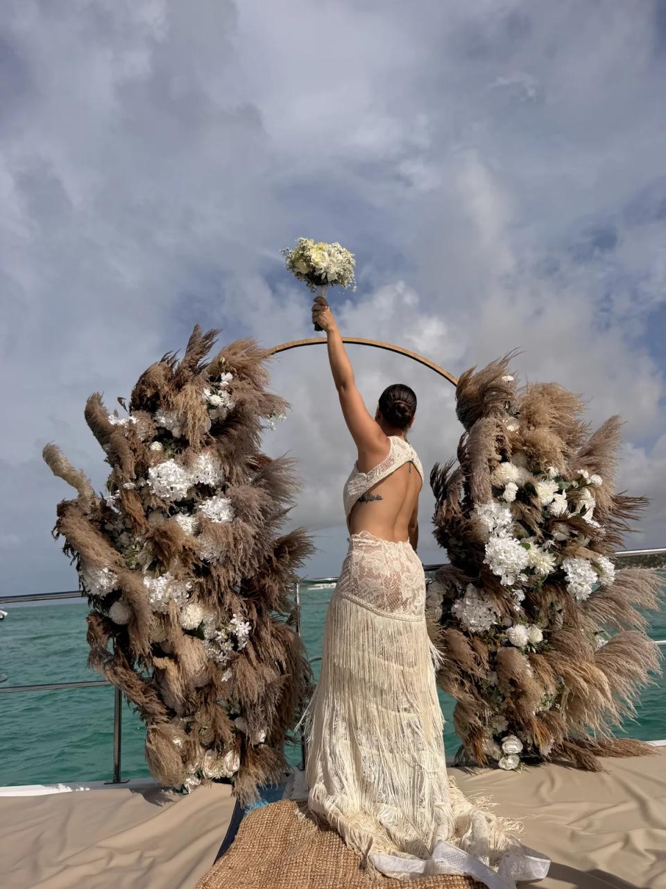 Mariée levant son bouquet près d’une arche de pampas sur un catamaran à Punta Cana