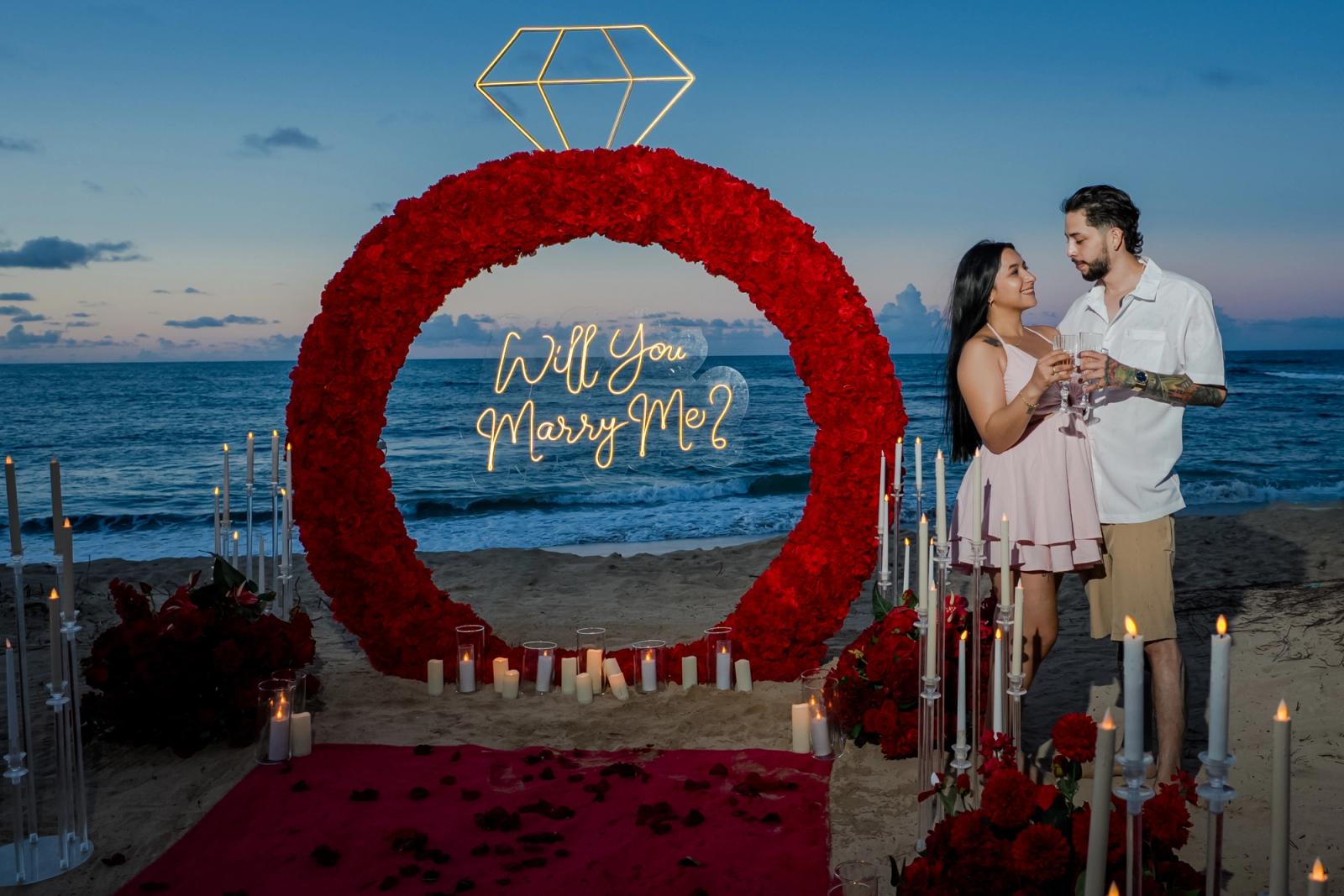 Endless Love: Couple beside the red floral engagement ring on the beach. Endless Love: Couple beside the red floral engagement ring on the beach.