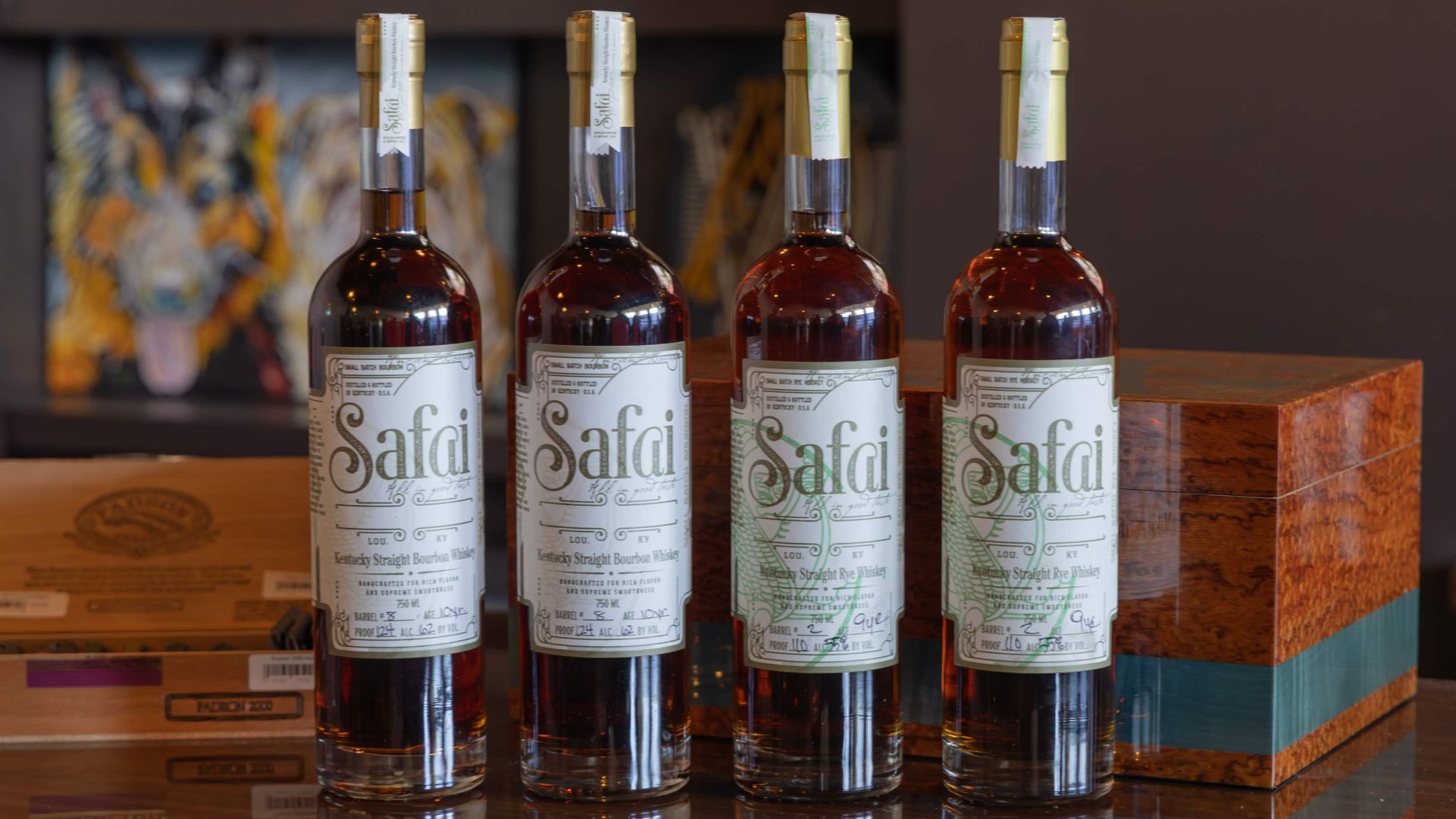 Four bottles of Safai Kentucky Straight Bourbon and Rye Whiskey displayed on a table beside a wood humidor
