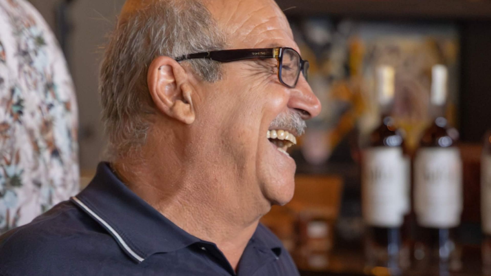 Mike Safai, founder of Safai Whiskey, laughing at an Orlando Whiskey Alliance event with Safai bourbon bottles displayed in the background