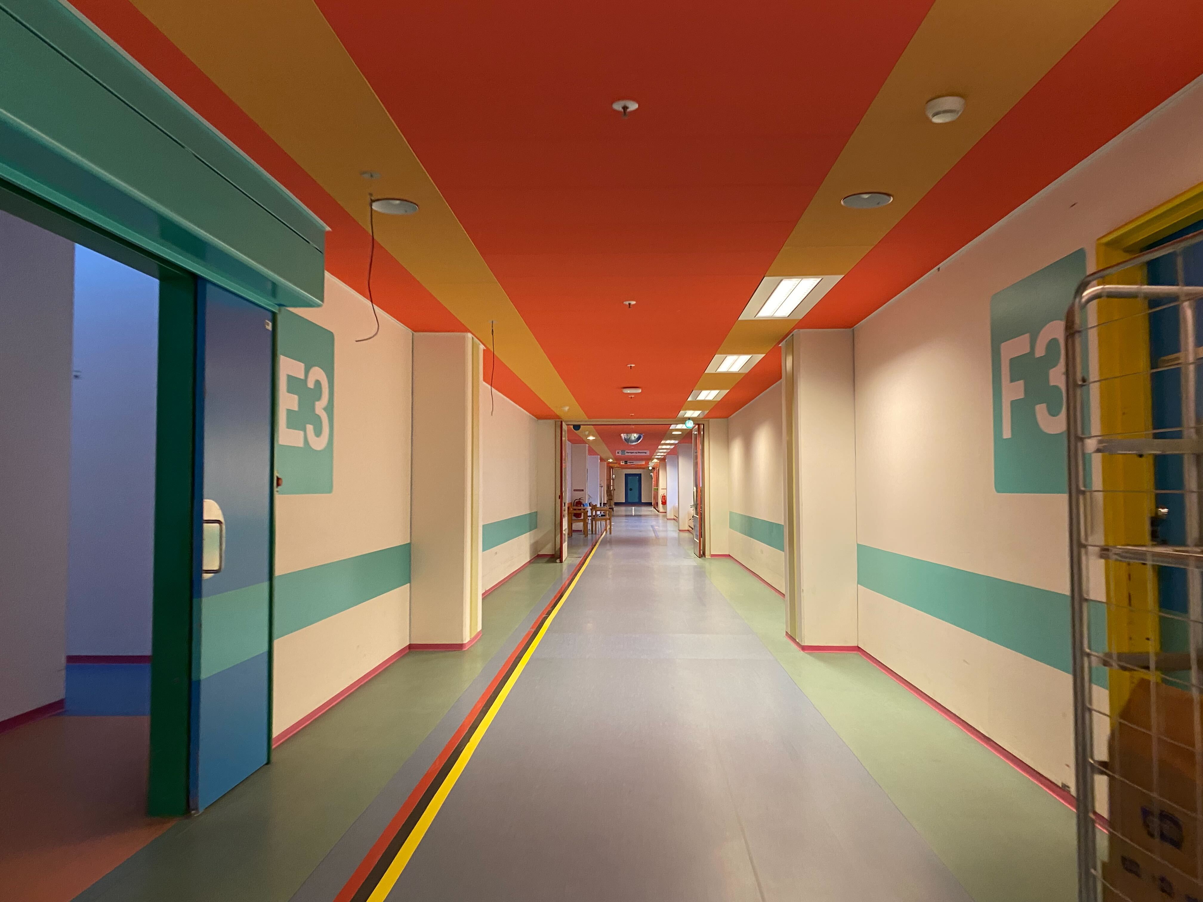 A long hallway at Herlev Hospital with a colorful orange ceiling and colorful stripes on the walls and floor. Design by Paul Gernes.
