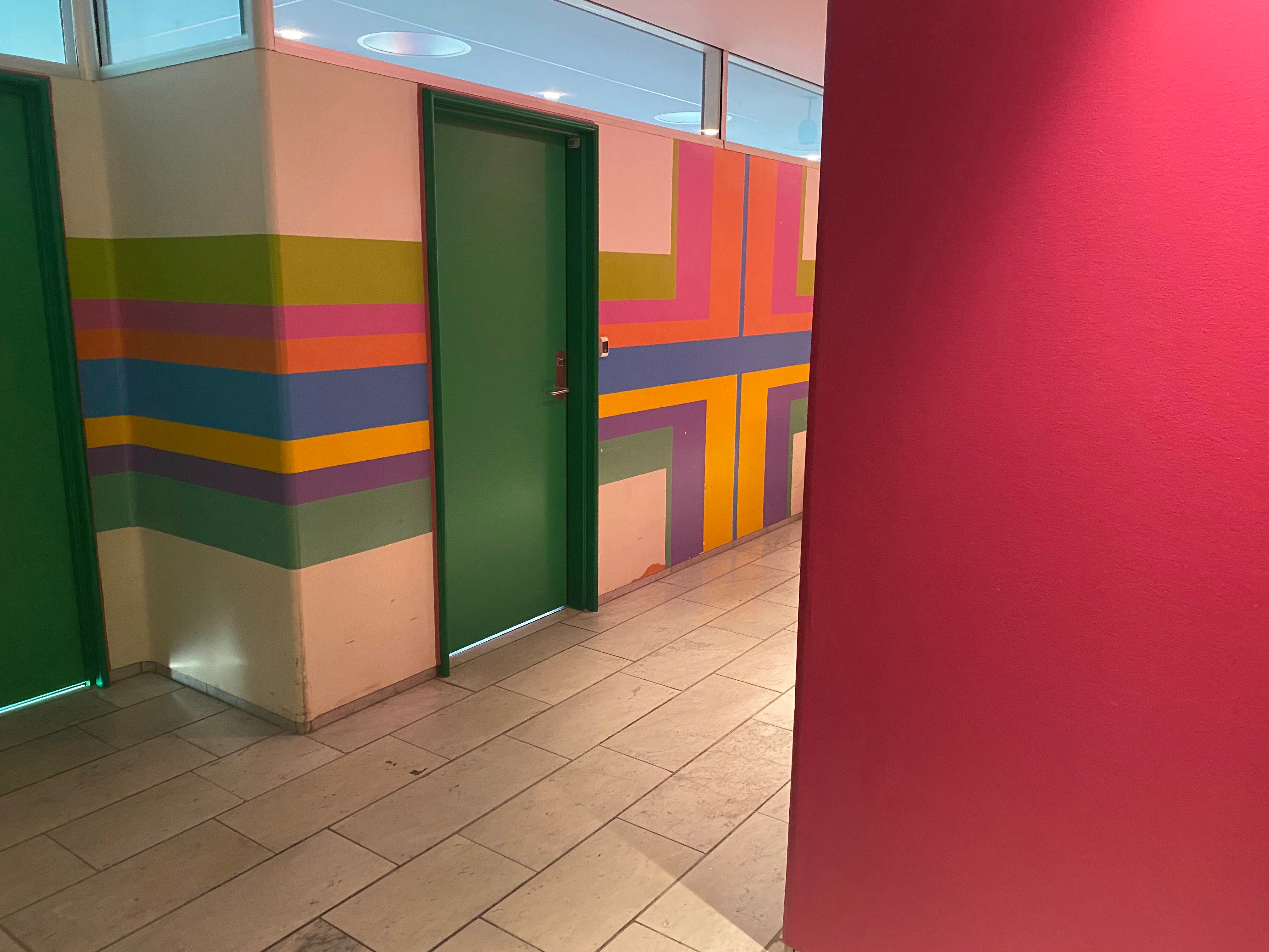 Photo from Herlev Hospital showing a hallway with green door and figurative painting in bright colors on the wall. Color design by Paul Gernes.