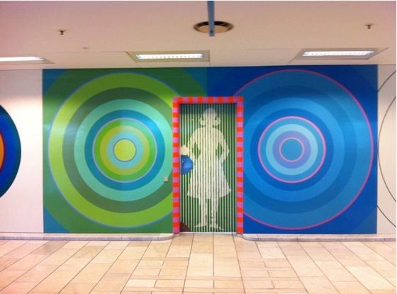 Photo of a wall painted in bright colors with large circles at Herlev hospital. A door leads to a ladies room. Color design by the Danish artist Poul Gernes.