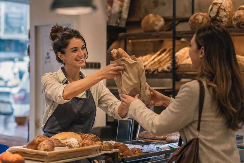 Bakery owner handing a bag of bread to a happy customer