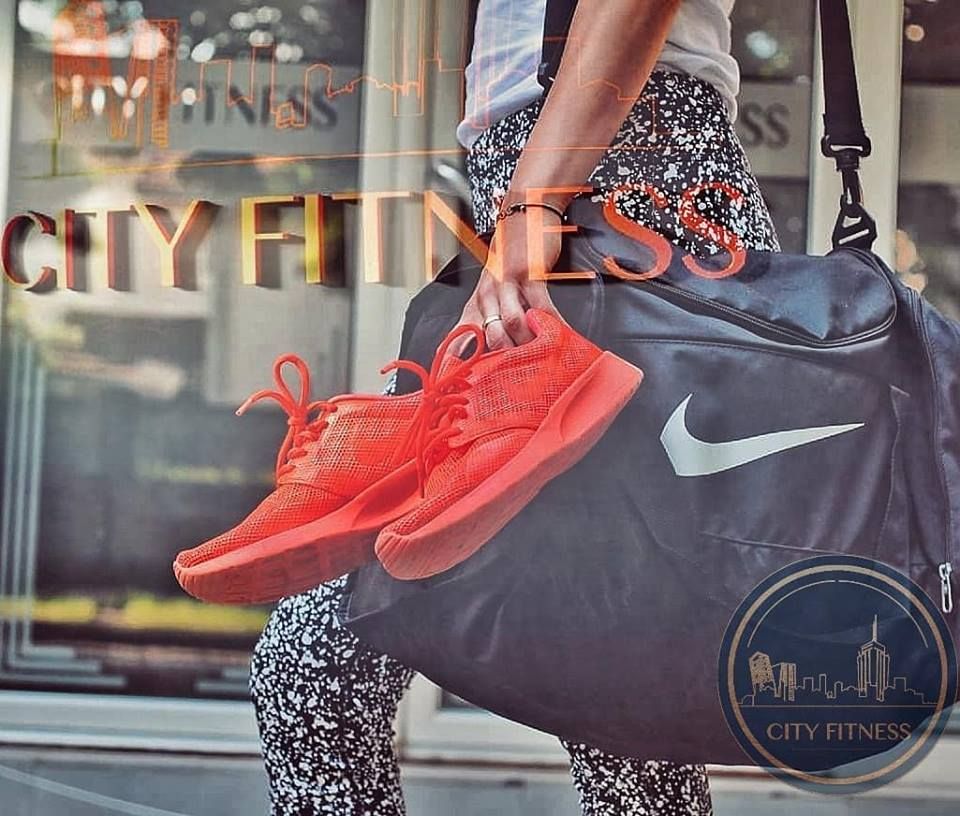 Žena koja nosi torbu i drži u ruci patike fotografisana ispred City Fitness centra