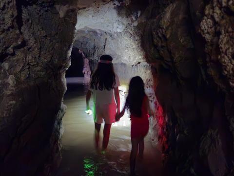 רומי ודניאל הולכות יד ביד בתוך נקבת אלונה, עם מקלות זוהר ומים עד הקרסול