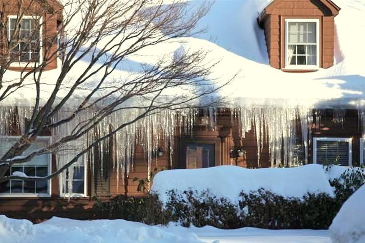 Heavy icicles and an ice dam hanging from the eaves of a snow-covered Boston-area house