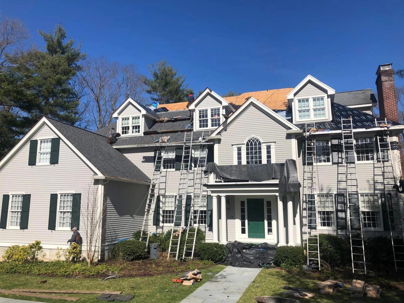 A large white colonial part-way through a re-roof, ladders and staging up the full height and the front slope stripped to bare deck