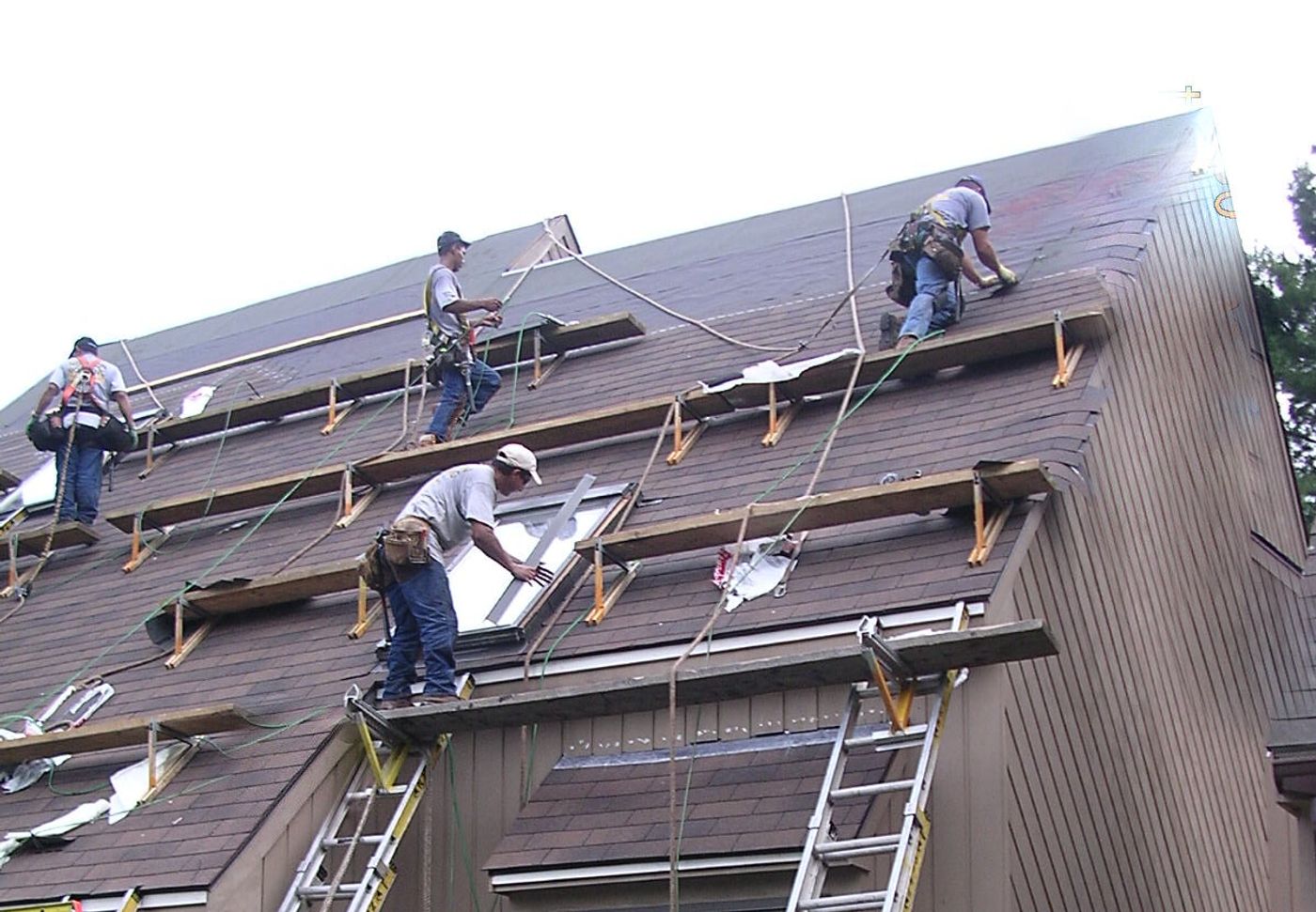 Crew on roof staging setting a new skylight into a steep shingle roof