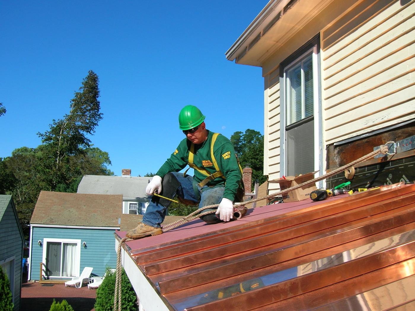 Newton Roofing crew member in a branded shirt measuring a standing seam copper panel on a porch roof