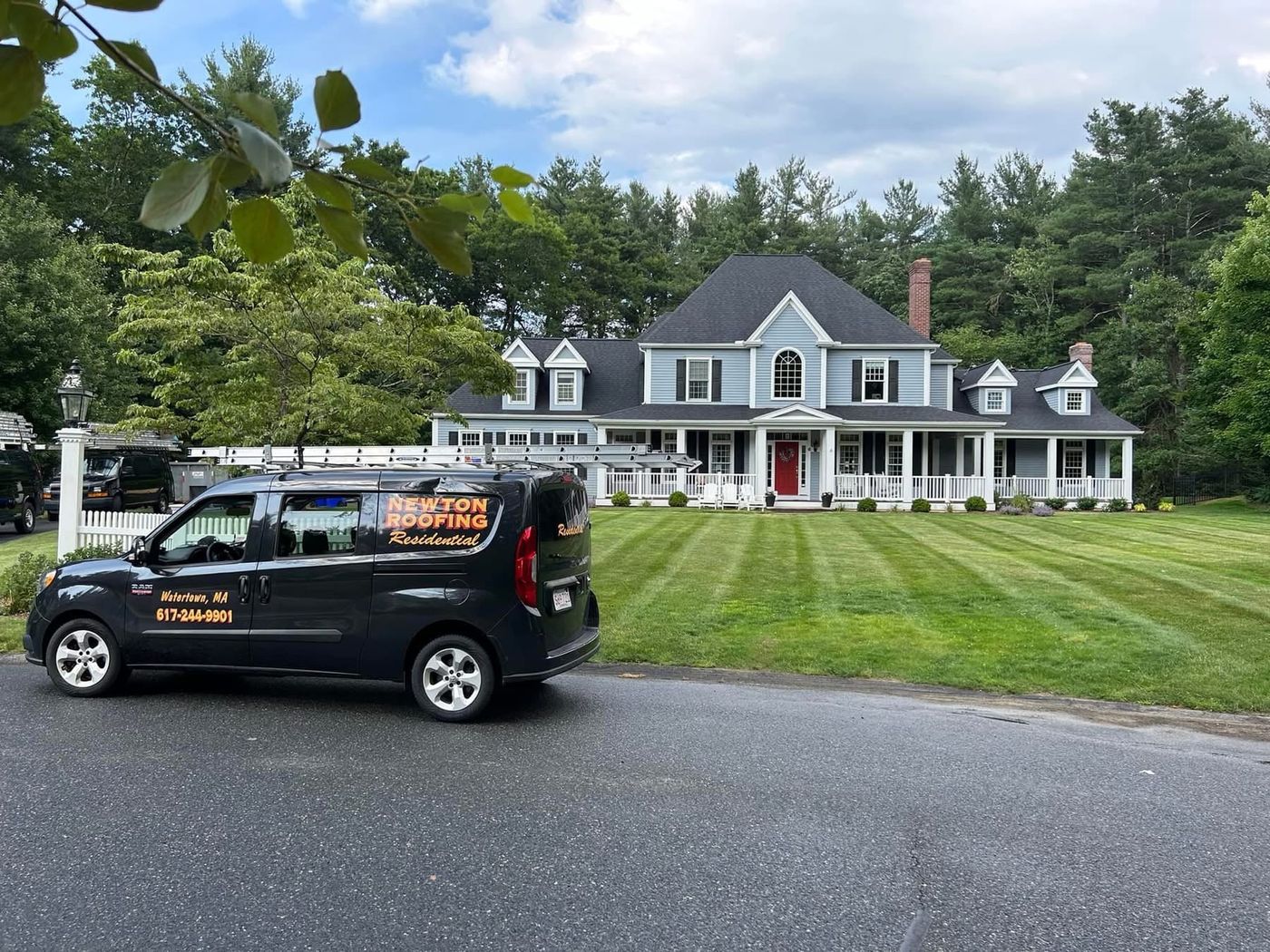 A Newton Roofing Residential van parked at the roadside in front of a large white colonial with a striped lawn