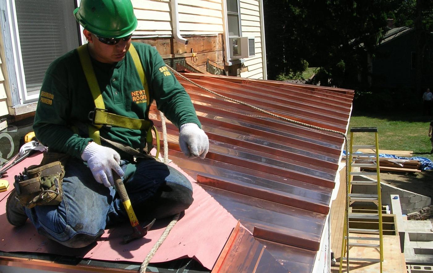 Newton Roofing crew member setting standing seam copper panels on a bay roof