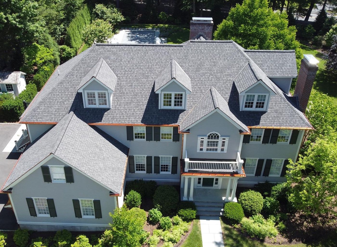 Aerial view of a completed gray architectural shingle roof with copper gutters on a colonial