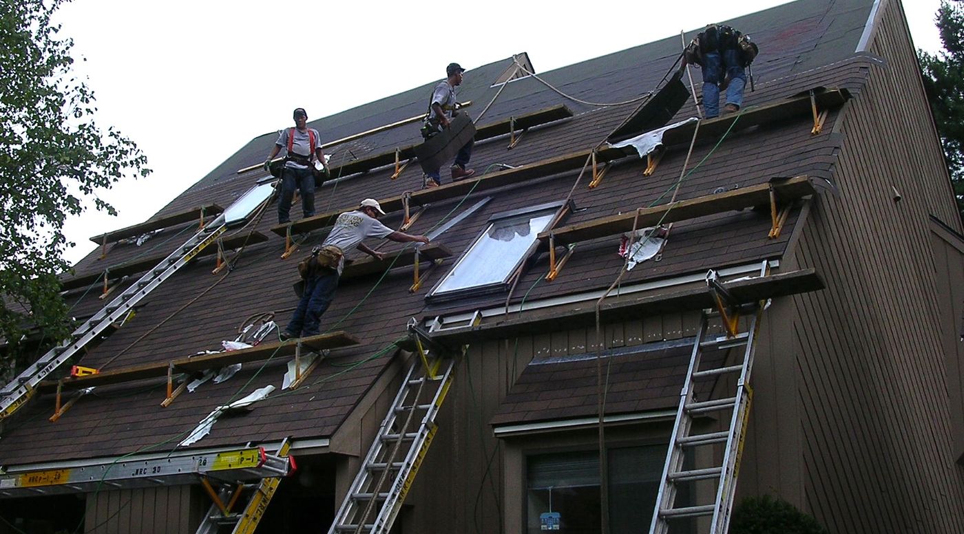Four-person crew on roof staging stripping shingles from a steep pitched roof