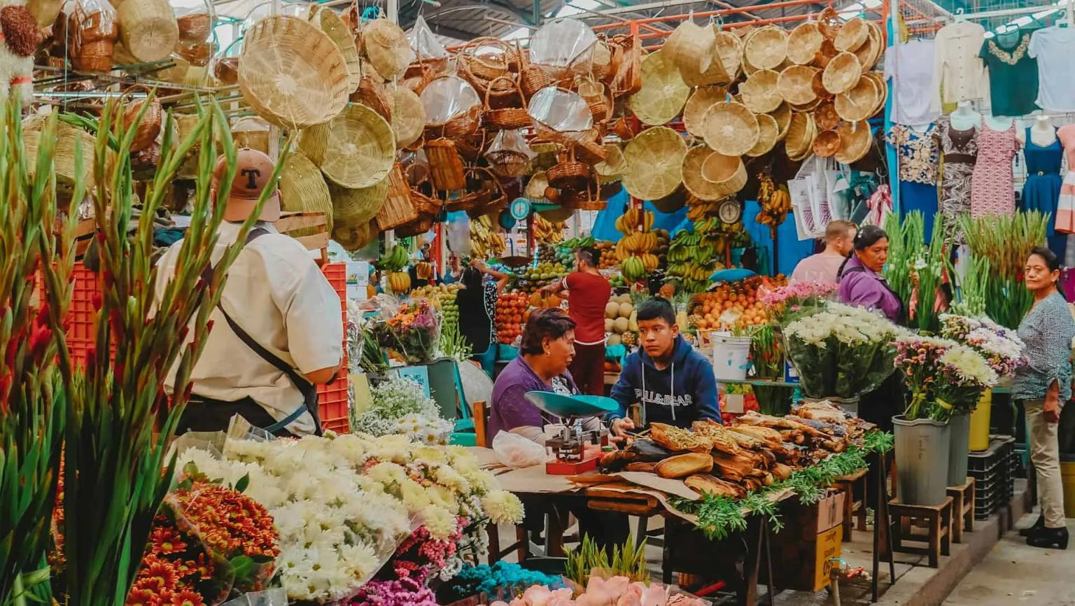 Mercado vibrante no México, com flores, frutas e artesanato expostos.