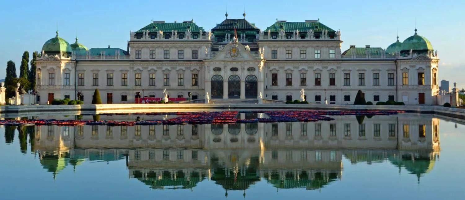 Palácio Belvedere refletido em lagoa, cercado por jardins bem cuidados.