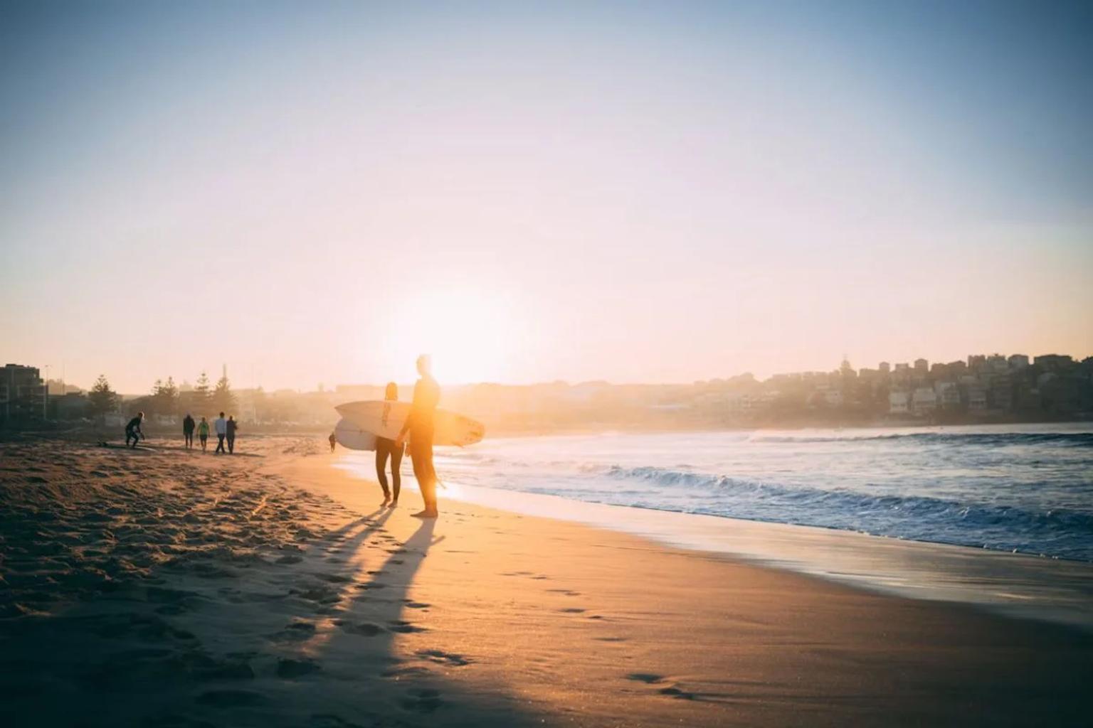 Seguro de viagem para a Austrália: surfista ao pôr do sol numa praia australiana