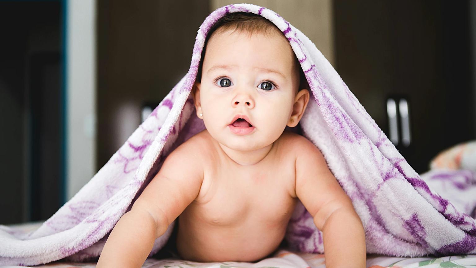 ¿Cuánto cuesta criar un hijo en España como el bebé de esta imagen que mira a cámara cubierto con una manta