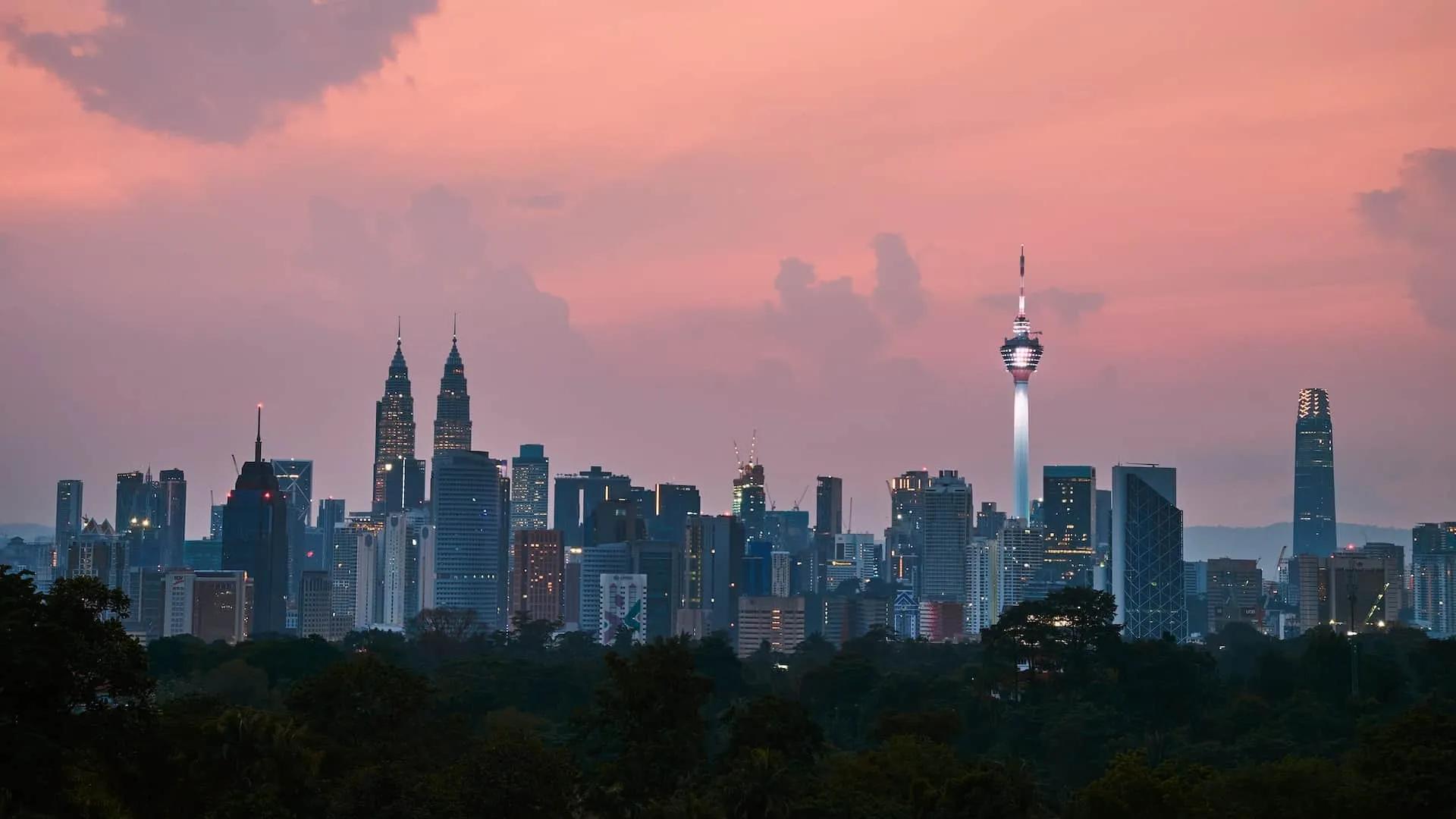 Vista panorâmica do skyline de Kuala Lumpur ao entardecer, com torres icônicas.