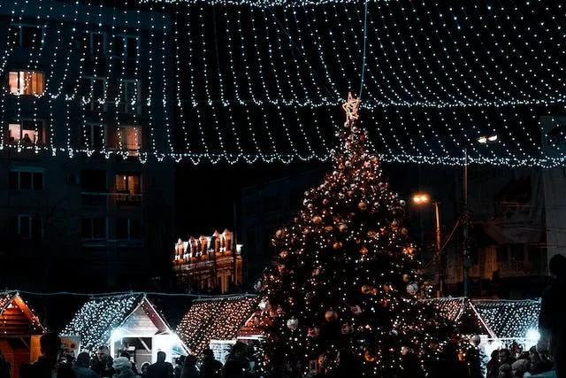 A decorated Christmas tree surrounded by festive lights and market stalls at night.