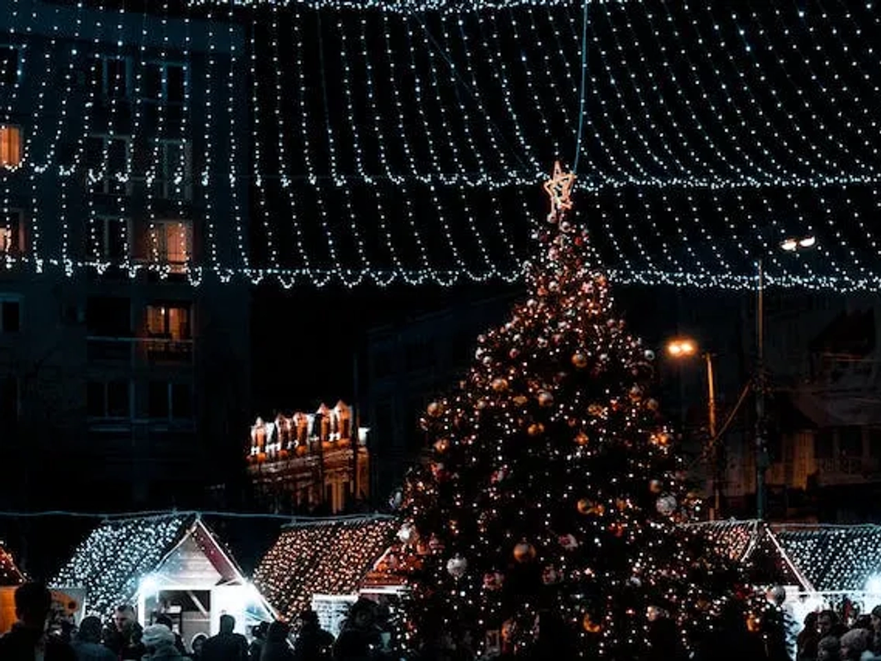 A decorated Christmas tree surrounded by festive lights and market stalls at night.