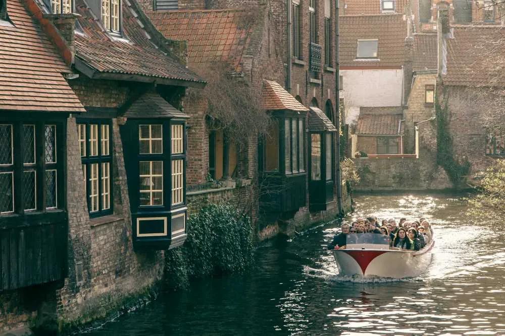 Grupo de turistas navegando en un canal rodeado de casas históricas en Bélgica.