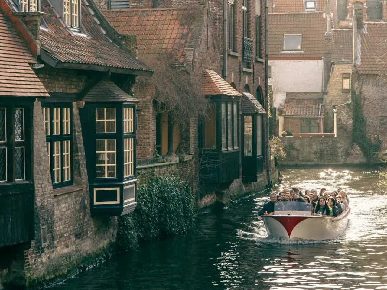 Grupo de turistas navegando en un canal rodeado de casas históricas en Bélgica.