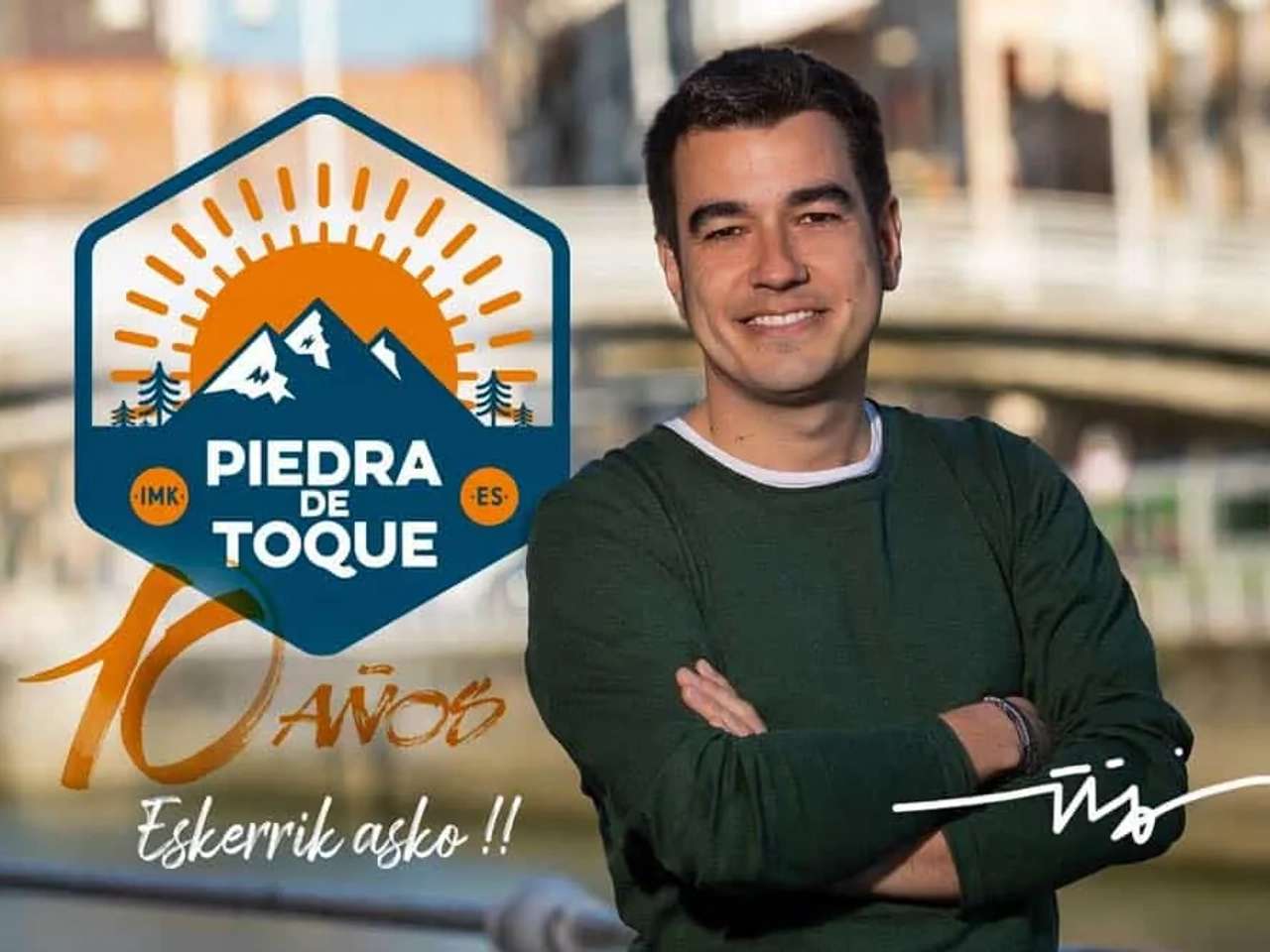 Hombre sonriente frente a un puente, con logo de "Piedra de Toque" y celebración.