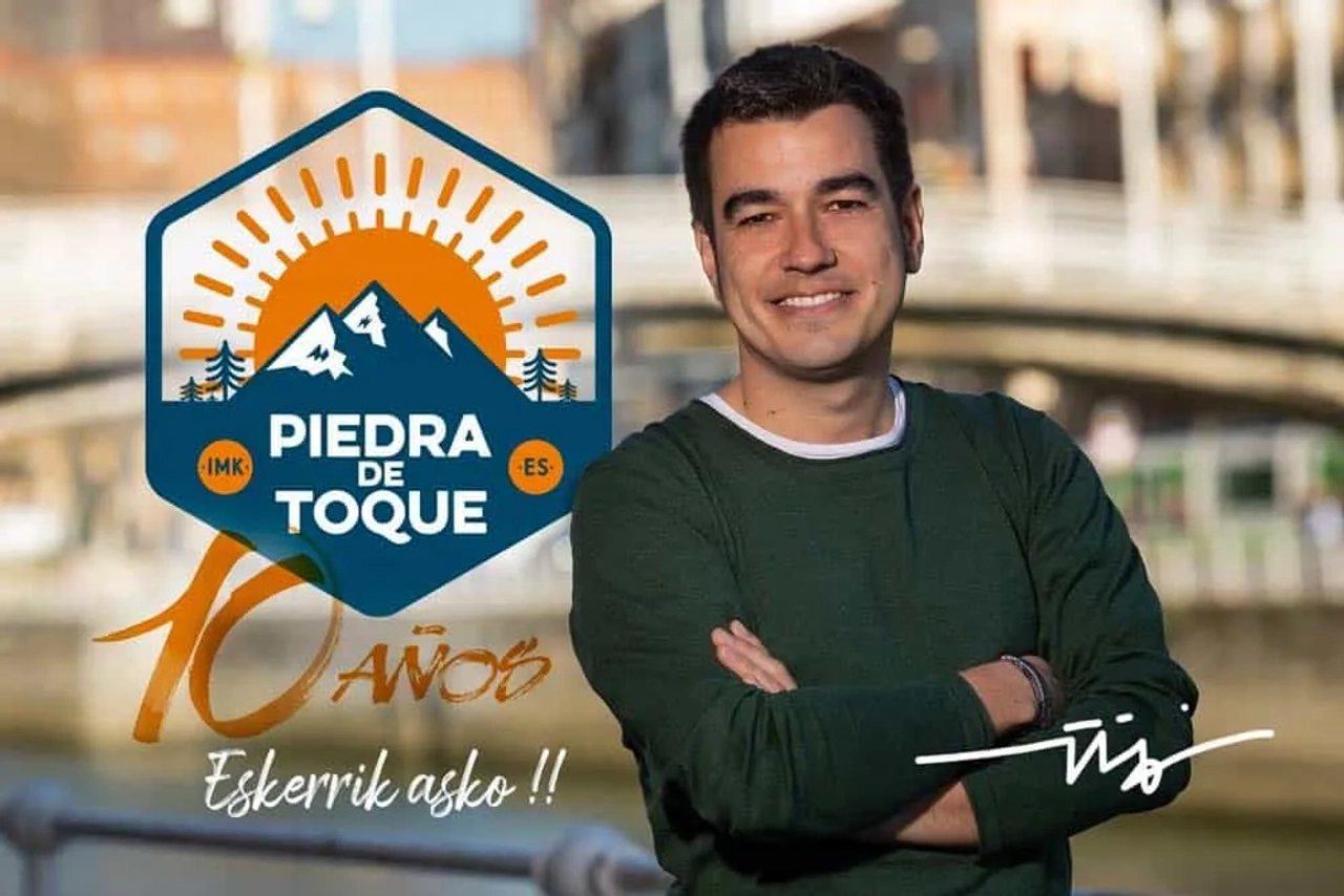 Hombre sonriente frente a un puente, con logo de "Piedra de Toque" y celebración.