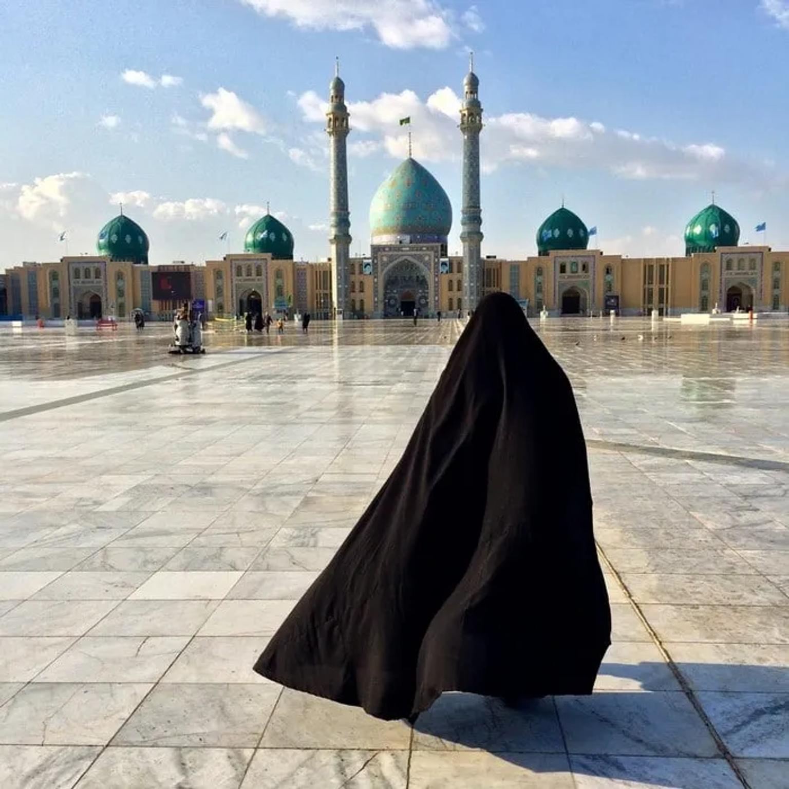 Mujer con chador frente a una mezquita con cúpulas verdes en Irán.