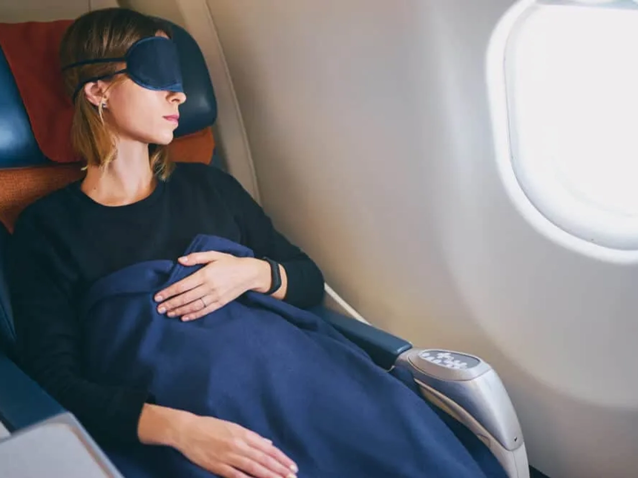 mulher deitada com manta e mascara num aviao