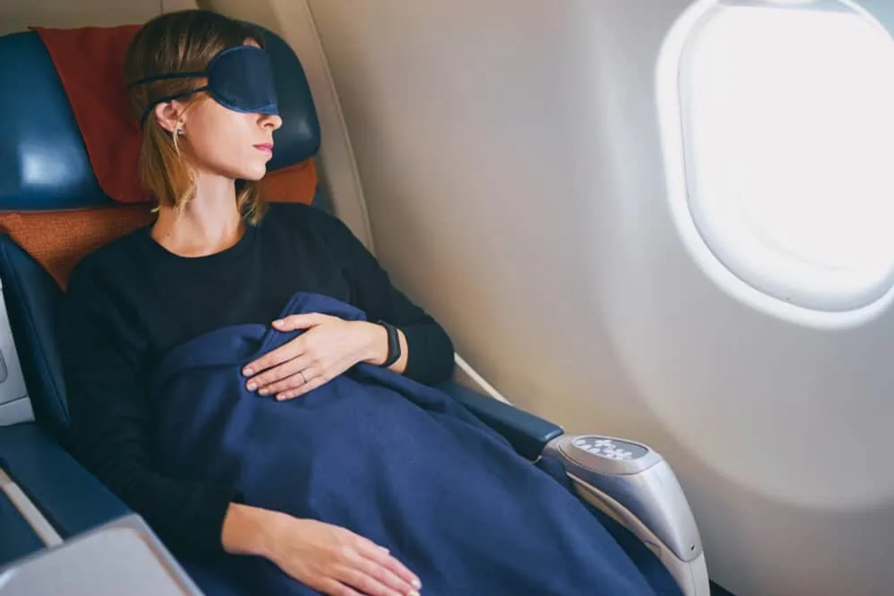 mulher deitada com manta e mascara num aviao