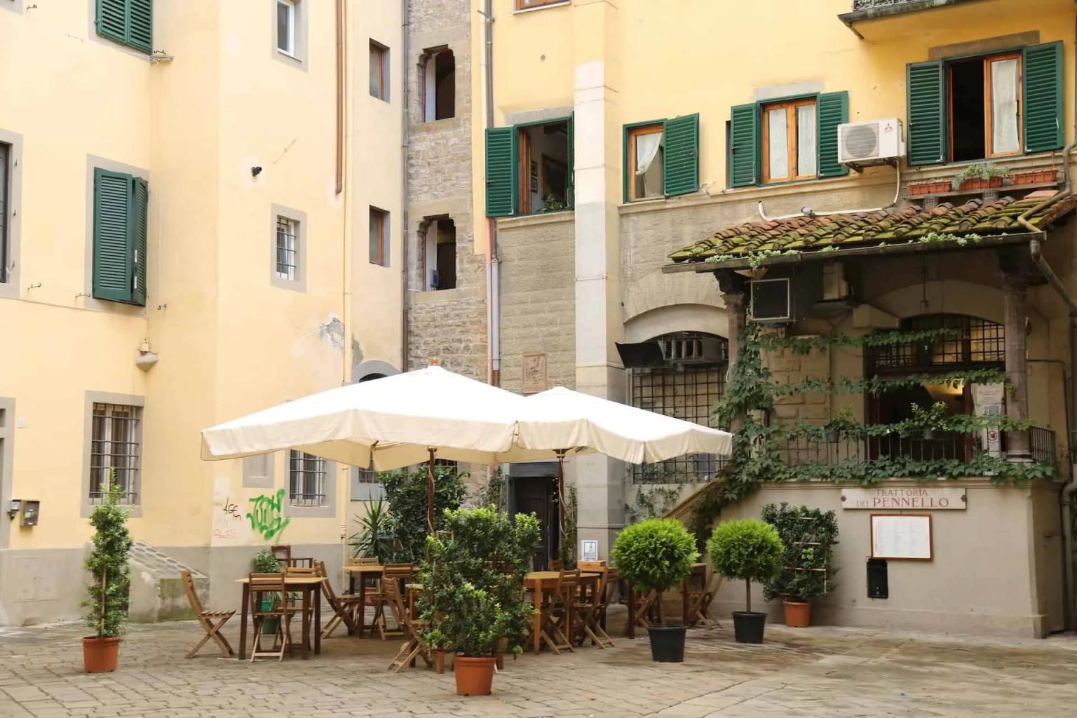 Charming outdoor dining area with tables, umbrellas, and greenery in a historic Florence courtyard.