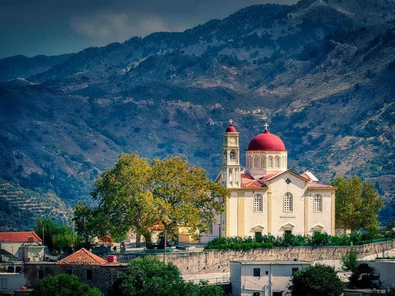 Igreja com cúpula vermelha em meio a montanhas na Grécia.