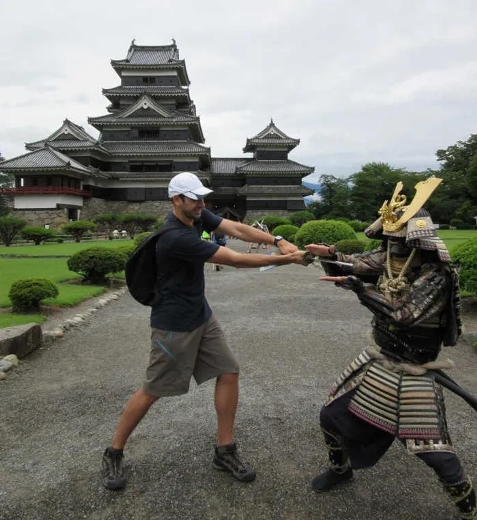 Hombre interactuando con un samurái frente a un castillo japonés.