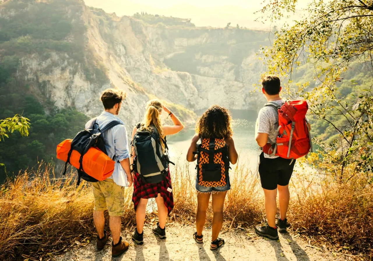 quatro jovens mochileiros olham para um rio desde uma montanha