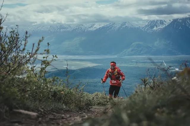 Corredor subiendo una montaña, con paisaje de montañas y valle al fondo.
