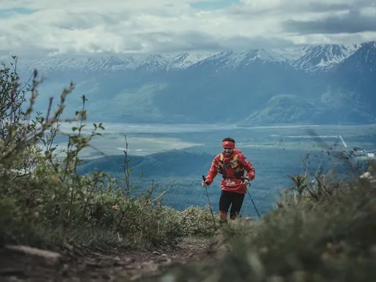Corredor subiendo una montaña, con paisaje de montañas y valle al fondo.