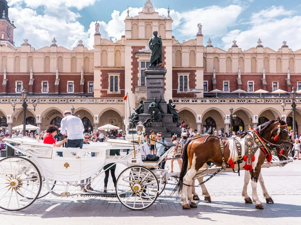Carruagem puxada por cavalos na praça principal de Cracóvia, junto aos edifícios históricos do centro.