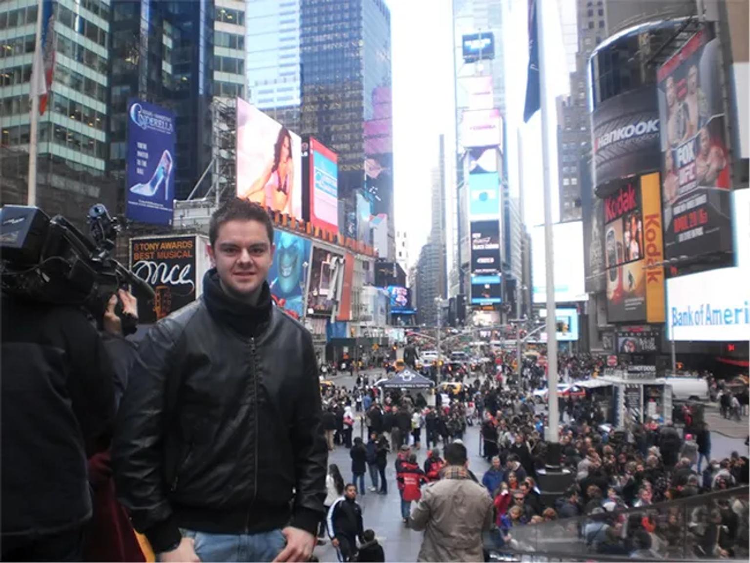 Hombre posando en Times Square, rodeado de multitudes y pantallas publicitarias.