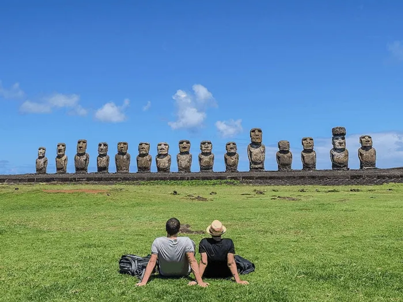 Pareja sentada frente a moáis en la Isla de Pascua bajo un cielo azul.