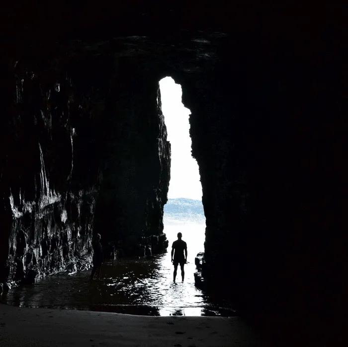 Siluetas de personas en una cueva con luz natural al fondo.