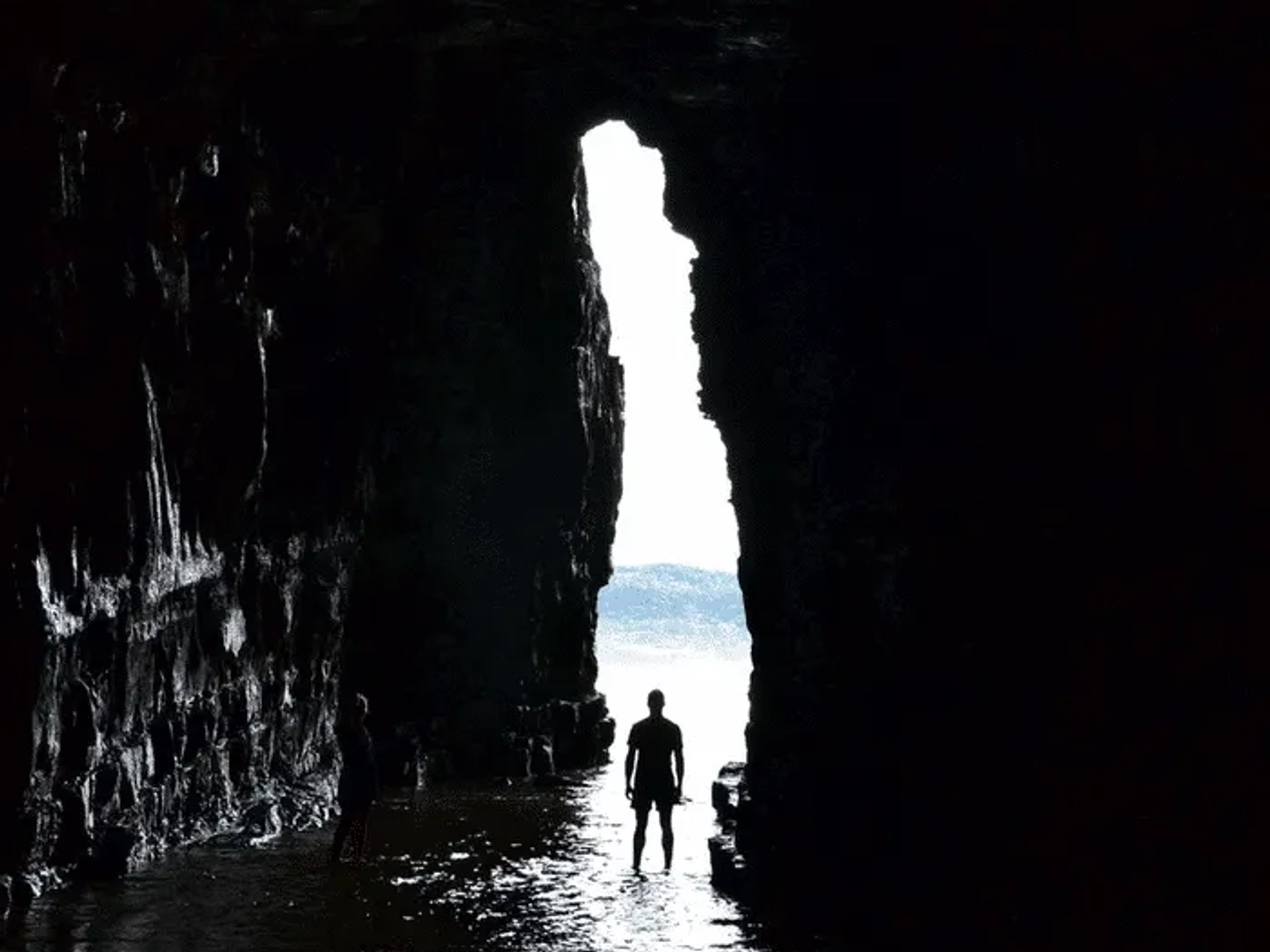 Siluetas de personas en una cueva con luz natural al fondo.