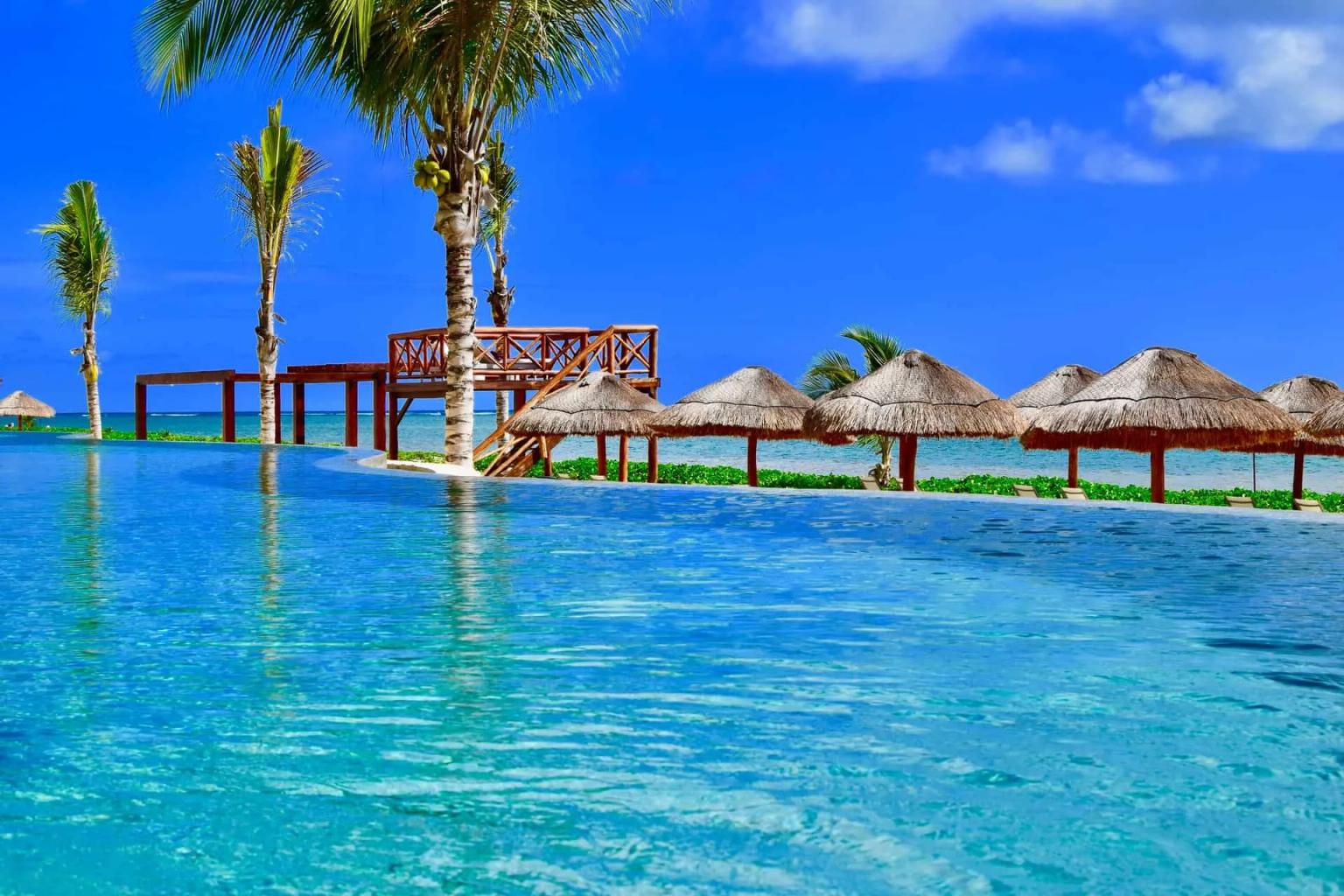 Piscina de borda infinita com palmeiras e bangalôs à beira-mar no México.