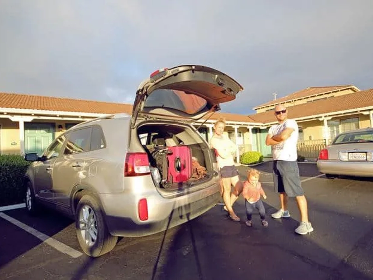Familia junto a un coche con maletas, frente a un motel.