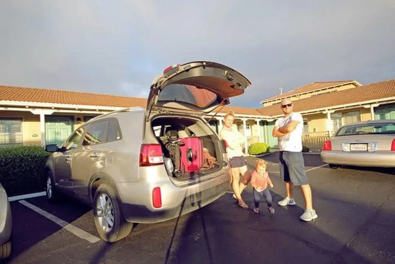 Familia junto a un coche con maletas, frente a un motel.