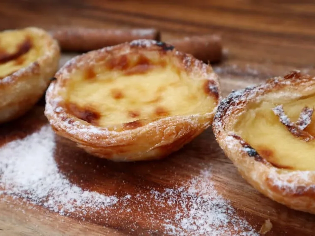 três pasteis de belem numa mesa de madeira