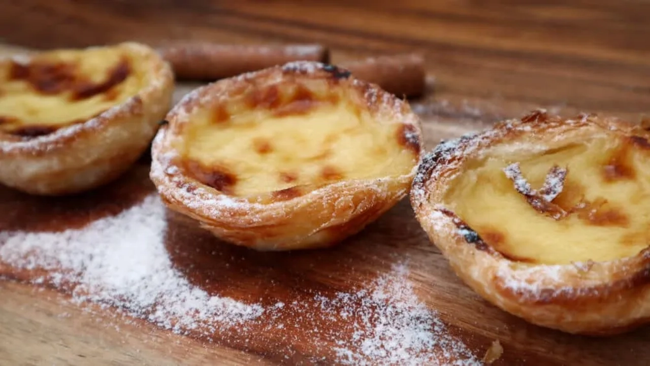 três pasteis de belem numa mesa de madeira